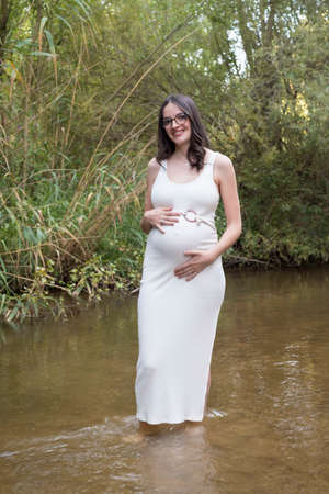 young pregnant woman sitting on a bench in the field.の写真素材