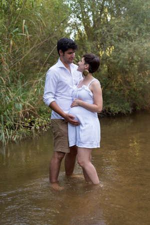 young pregnant woman, with her partner, sitting on a bench in the field.の写真素材