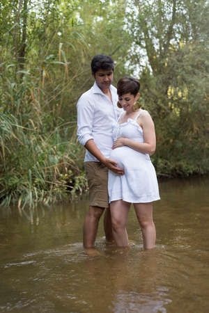 young pregnant woman, with her partner, sitting on a bench in the field.の写真素材