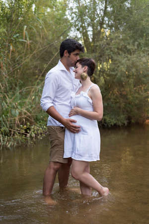 young pregnant woman, with her partner, sitting on a bench in the field.の写真素材