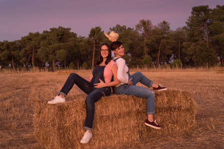 The cheerful Caucasian women on maternity shoot sitting on hay in a fieldの写真素材