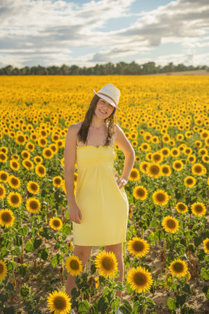 A young woman dressed in yellow and wearing a hat in a field of sunflowersの写真素材