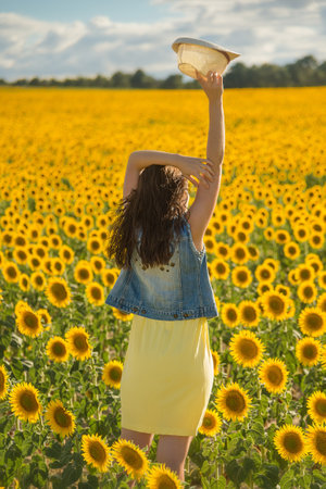 A young woman dressed in yellow and holding a hat in her hand in a field of sunflowersの写真素材