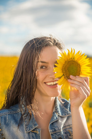 A young woman with a sunflower in front of her eyes in a field of sunflowersの写真素材