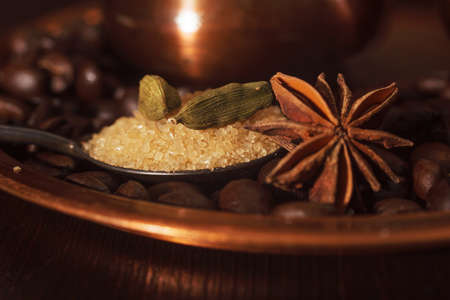 Closeup of cardamom pods, anise and brown sugar in a teaspoon with coffee beans and shiny copper plate and pot as a background.の写真素材