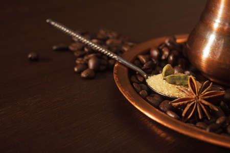 Closeup of cardamom pods, anise and brown sugar in a teaspoon with coffee beans and shiny copper plate and pot as a background.の写真素材