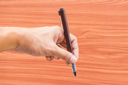 Hand holding a pen with wooden background, Main focus on handの写真素材