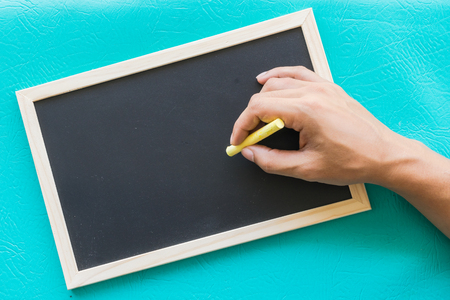 Blank blackboard with blue background, Hand writing on blackboard, Main focus on handの写真素材