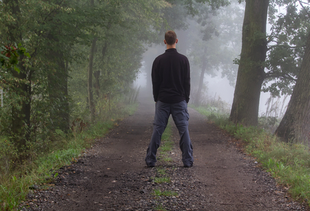 Young man standing on path in morning misty fogの写真素材