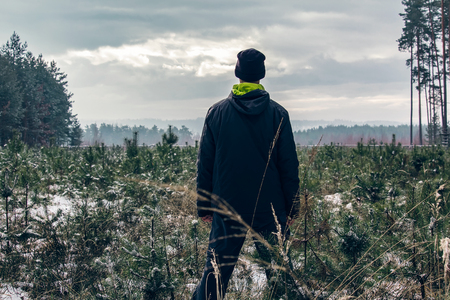 Young man standing in winter in forest with snow and dramatic skyの写真素材