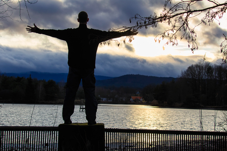Silhouette of young man standing on outlet of pondの写真素材