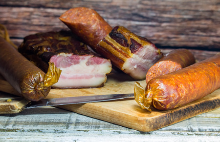 Bacon and sausage on white wood background with knife