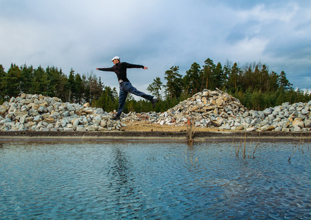 Young man jump near waterwith stone and forest