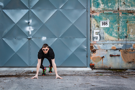 Handsome young man, runner in start position from front with door and rough wall. Fitness, workout,...
