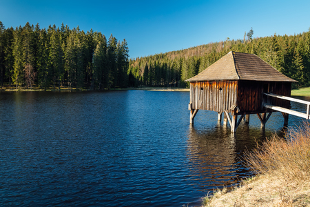 Wooden building on pond with trees and blue skyの写真素材
