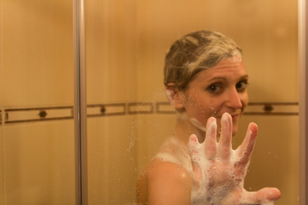 Beauty young caucasian blonde woman shower in bath touch on glass with shampoo