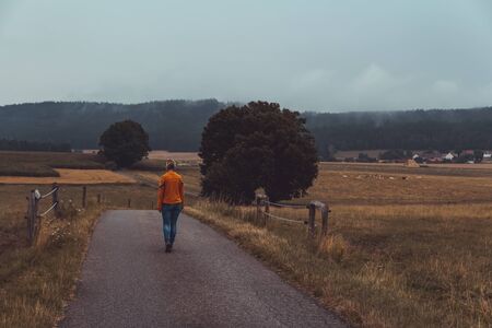 Young woman walk in Czech rural landscape in rain weather in orange shirtの写真素材
