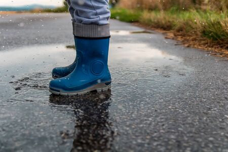 Young boy jump into puddle with gumboots and splash water on streetの写真素材