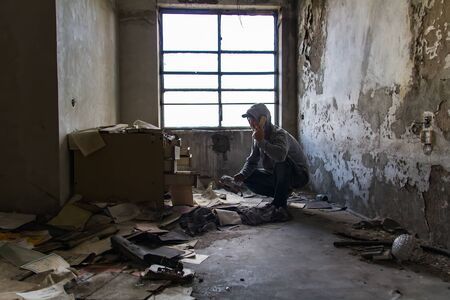 Caucasian man in cap and hood phone with broken phone in abandoned building. Hacker, racketeer, terrorist conceptの写真素材