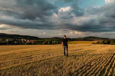 Young man walking on mowed field with dramatic sky at sunset, Czech republicの写真素材