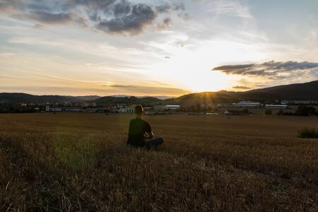 Young man sitting on mowed field at sunset, Czech republicの写真素材