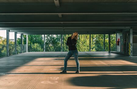 Beautiful blonde caucasian young woman standing in garage, looking up. Urban concept, copy spaceの写真素材