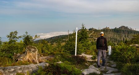 Young man tourist in white cap walking on footpath, hill Tristolicnik, Sumava National Park and...