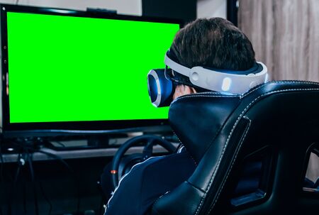 Young man play game with virtual reality glasses on simulator chair and steering wheel. Chroma key...