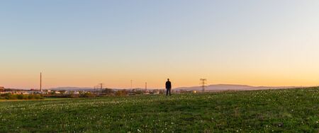 Caucasian man from back looking to industrial part of city Ceske Budejovice on meadow at sunset....