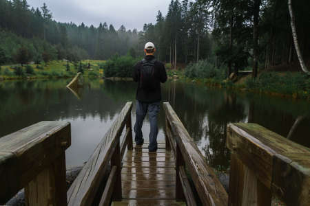 Young man standing on loodgate pond in rainy weather. Natural reserve Czech canada, dark mood green
