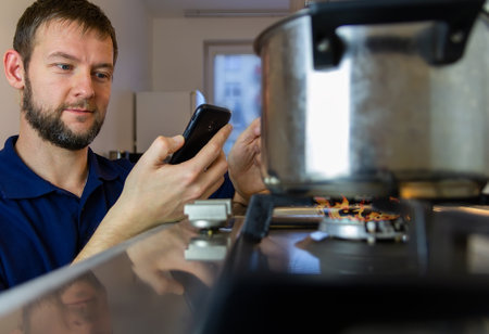 Young caucasian man happy, easy cooking in home kitchen with mobile phone. Man making home works...