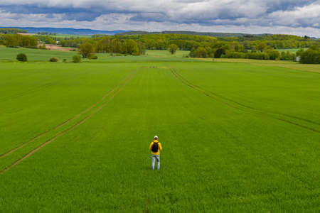Aeirial view young caucasian man from back with backpack walking on spring green agriculture field. Czech landscapeの写真素材