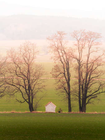Small chapel between trees in morning fog with distant hill. Czech landscape, spring valleyの写真素材