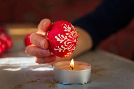 Close up photo of woman hand remove wax from easter egg with candle fire. Tradition method of paintingの写真素材