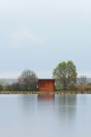 Wooden cabin, building on pond shore in rain moody weather. Long exposure, Czech landscapeの写真素材