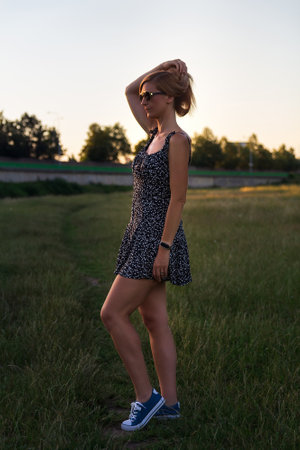 Portrait young blonde woman from side with sunglasses holding her hair, posing at sunsetの写真素材