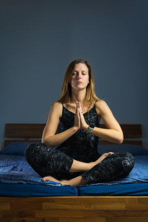 Beauty young Caucasian woman sitting in yoga position on bed. Relaxing routine before or after sleepingの写真素材