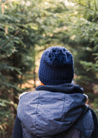 Young woman from back with redhead in knitted hat walking in forestの写真素材
