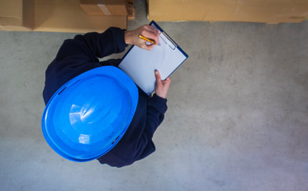 Top down view of warehouse worker in helmet checking box with pen and paper. Stock of Parcels with Products, transportation conceptの写真素材