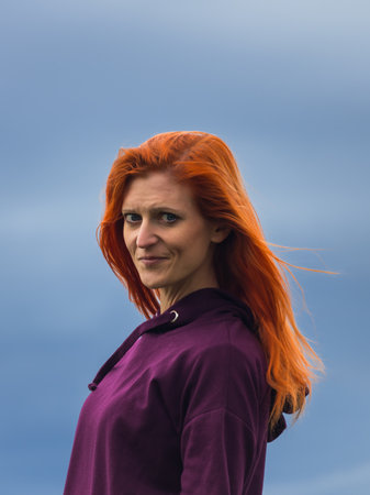 Portrait of red-headed smiling young woman against blue cloud