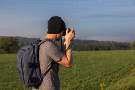 Traveler, photographer taking photo of Czech spring landscape with fog. Man in hat, shirt with backpack from backの写真素材
