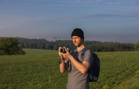 Traveler, photographer taking photo of Czech spring landscape with fog. Man in hat, shirt with backpack looking into sunの写真素材
