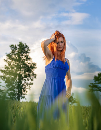 Portrait of young woman in blue dress posing in agricultural fieldの写真素材
