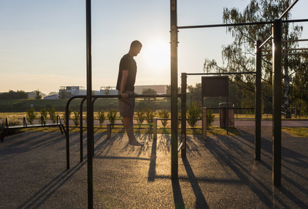 Fitness man doing dips on the work out playground at sunrise. Morning routine, mental and physical strength, healthy lifestyle backgroundの写真素材