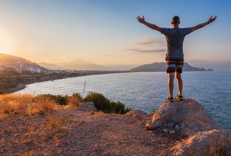 Man from back standing on rock with hands up, enjoy looking to city Alanya, Turkeyの写真素材