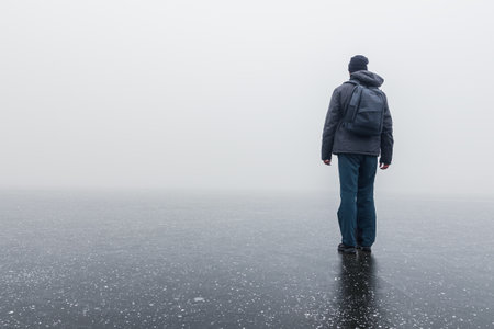A man with a backpack on his back standing on a frozen pond in the fogの写真素材