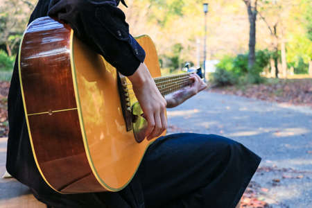 Woman playing acoustic guitar on park bench