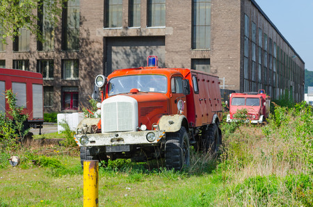 Old abandoned fire truck on a meadow in front of an old factory building 