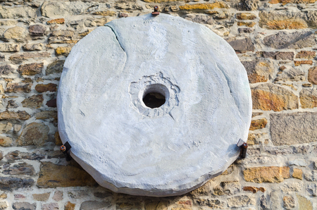 Traditional old millstone hung on a dry stone wallの写真素材