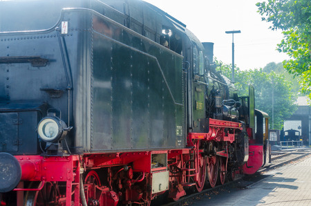 Exit and back view of a steam locomotive under full steam at the exit of a train station.